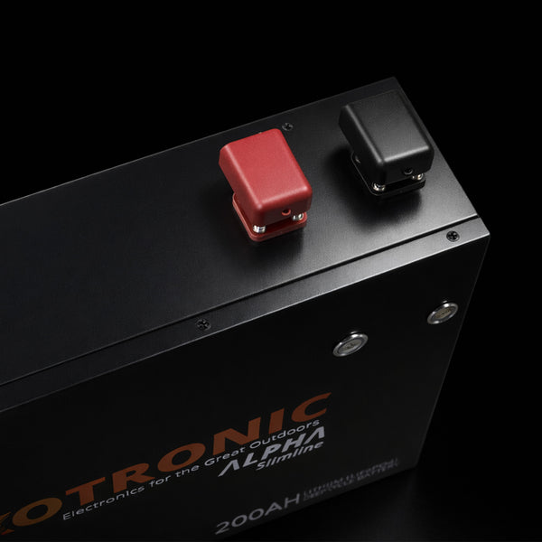 High-angle close-up of red and black M8 battery terminals with protective covers on top of black metal casing