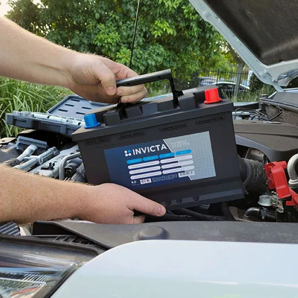 Mechanic lowering the Invicta lithium battery into a vehicle engine bay using the integrated handle