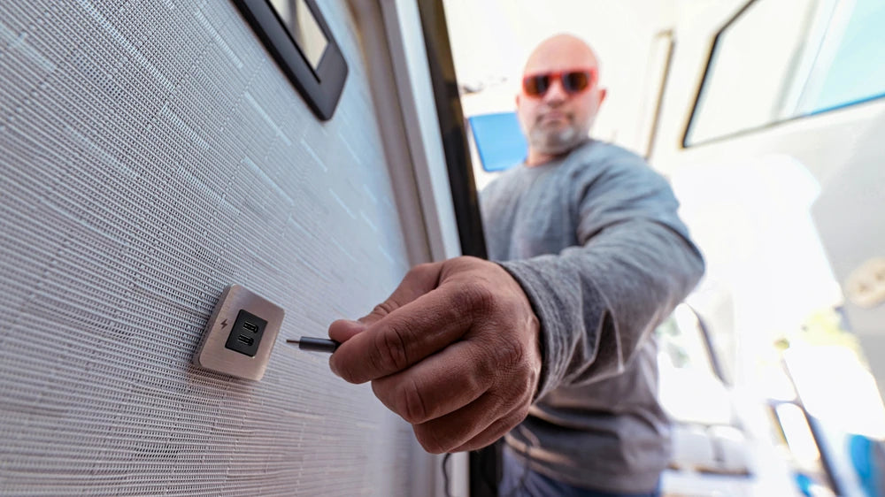 Hand plugging a USB-C cable into the installed brushed stainless socket in a boat cabin