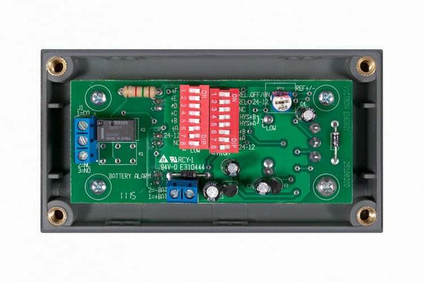 Internal view of battery alarm showing PCB with DIP switches and terminal blocks