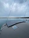 Two rectangular solar panels installed flat on the curved cabin roof of a boat anchored in calm water