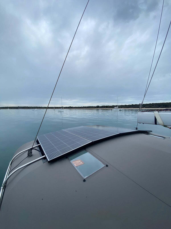 Two rectangular solar panels installed flat on the curved cabin roof of a boat anchored in calm water