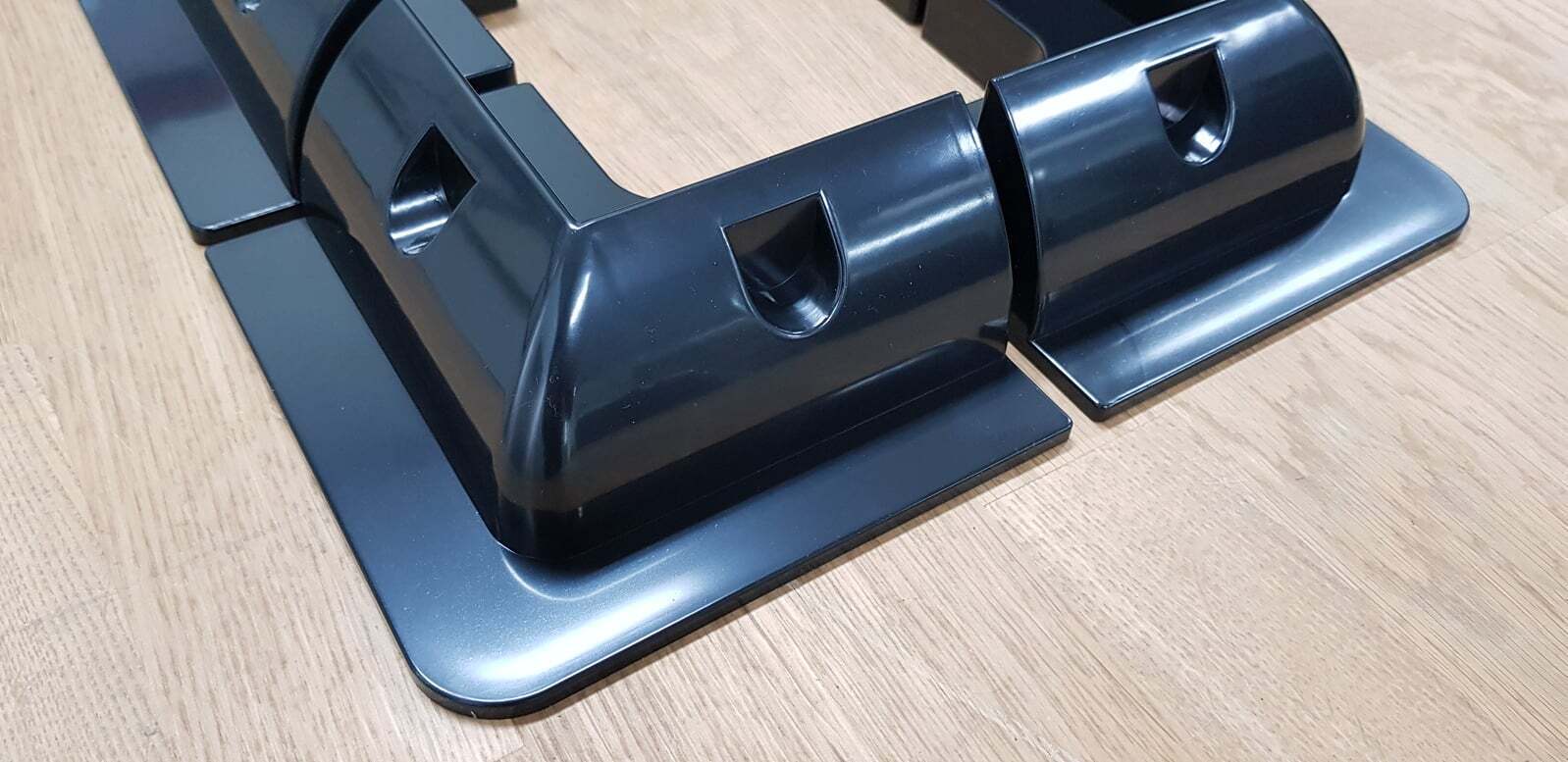 Close-up of black plastic corner bracket showing curved profile and recessed mounting holes