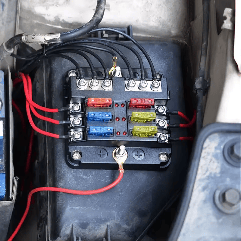 Automotive fuse block installed in engine bay with connected wiring and inserted blade fuses