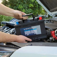 Hands lowering the lightweight Invicta lithium battery into a vehicle engine bay