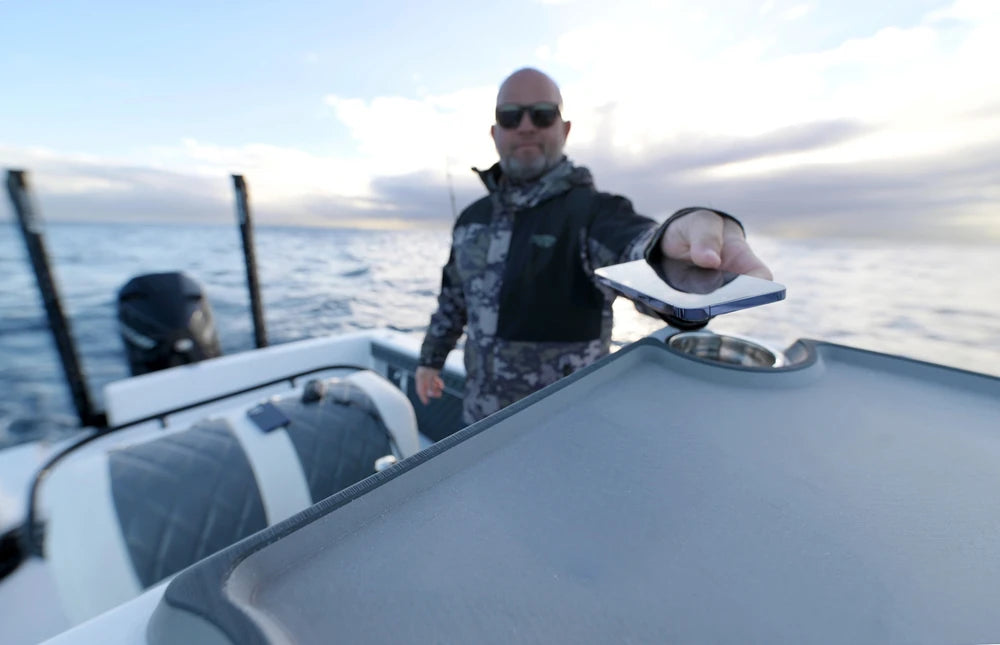 A smartphone being placed on a boat dashboard for wireless charging via a hidden sub-surface charger