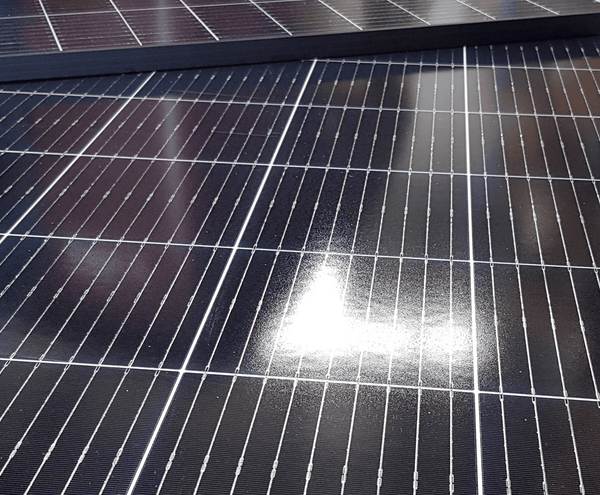 Close-up angled view of solar panel surface showing grid lines on black cells and tempered glass texture
