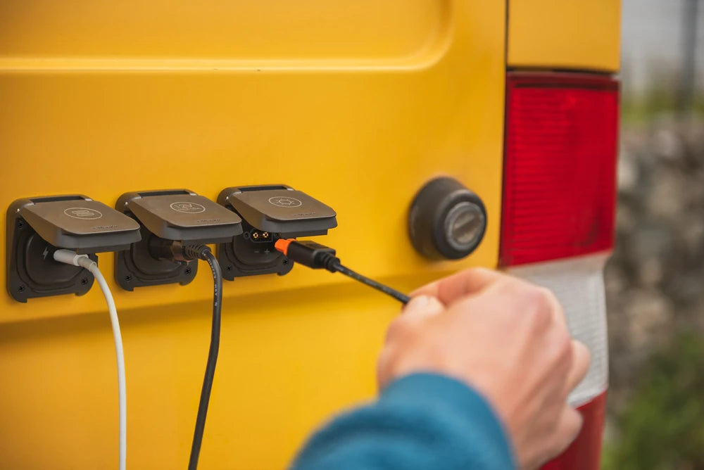 A user plugging a USB-C cable into the waterproof socket on the side of a campervan